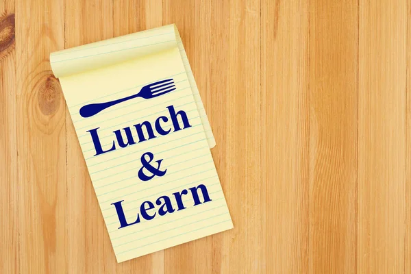 Lunch and Learn message with a fork on a yellow legal notepad paper on wood desk