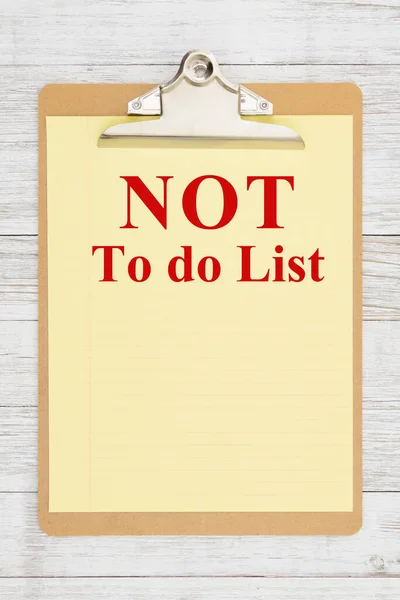 Not To Do List Message on yellow legal paper on a clipboard on weathered whitewash wood