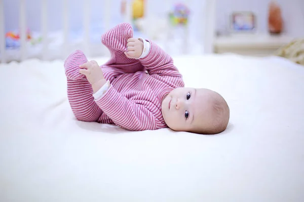 Niedliches kleines Baby spielt mit seinen Beinen auf dem Bett im Schlafzimmer — Stockfoto