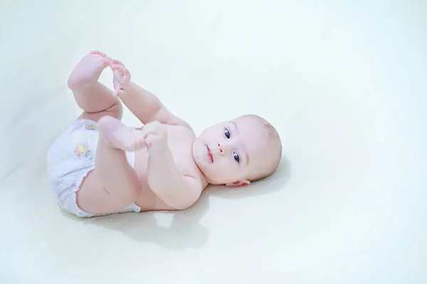 Lindo bebé niño usando pañal jugando con sus pies en la cama en — Foto de Stock