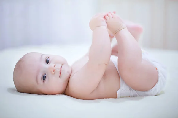 Söt baby spädbarn pojke bär blöja spela med fötterna i sängen — Stockfoto