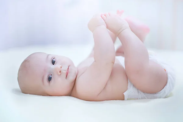 Rolig liten baby pojke bär en blöja som spelar på en vit blanke — Stockfoto