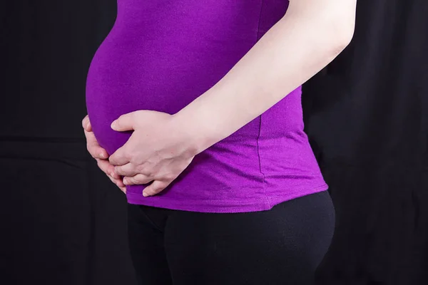 Primo piano di donna incinta con mani sopra la pancia a dorso nero — Foto Stock