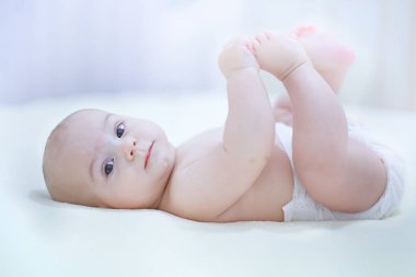 Funny little baby boy wearing a diaper playing in a sunny bedroo clipart
