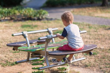 Güzel kıvırcık saçlı, 3 yaşındaki çocuk sallanan sandalyede oynuyor. Boş zaman konsepti. Yumuşak odaklanma. Yaz zamanı..