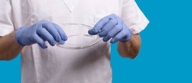 Büyüleyici cerrah, koronavirüs döneminde kişisel koruyucu ekipmanlarıyla ameliyathaneye girmeye hazırlanıyor. Tıbbi eldiven ve gözlük. Mavi arka plan. Metin için metin alanı olan pankart.