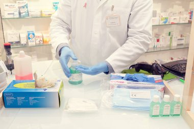 Brescia, İtalya, 10 Nisan 2020. Tıbbi maskeli ve eldivenli doktor eczanede çalışıyor, elleri dezenfekte ediyor. Covid-19 karantinasını tamamlamak için sağlık standartlarına saygı