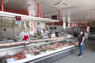 Brescia, İtalya, 11 Nisan 2020. Coronavirus salgını sırasında eldiven ve tıbbi maske takan kasap bir müşteriye et servisi yapıyor. Alışveriş, Covid-19 karantinası.