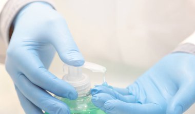 Doktorların yakın çekimleri ve koruyucu tıbbi eldivenleri, hastanın ve kendisinin güvenliği için jel ile dezenfekte ediyorlar. Enfeksiyondan kovid 19 'a kadar koruma. Yumuşak odak ve mavi arka plan. El dezenfektanı