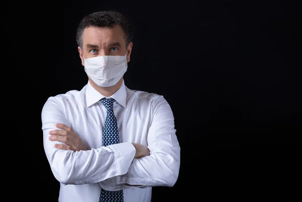 businessman with protective mask, dressed with white shirt and tie standing with arms crossed on black background. copy space for text