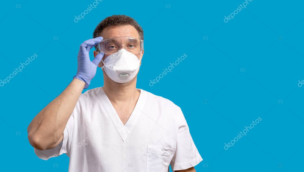 Coronavirus and medicine concept. Man wearing protective mask, glasses and blue latex gloves isolated on blue background. Banner with copy space.