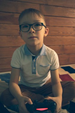 Gözlüklü beyaz çocuk elinde joystickle yatağında oturuyor..