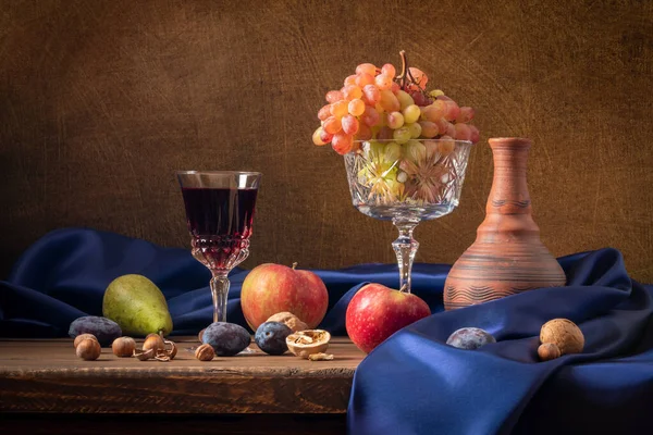 Натюрморт з фруктами та червоним вином. Виноград, яблука, груша, сливи, горіхи і синя драпірування — стокове фото