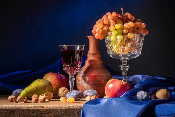 Натюрморт з фруктами та червоним вином. Виноград, яблука, груша, сливи, горіхи і синя драпірування — стокове фото