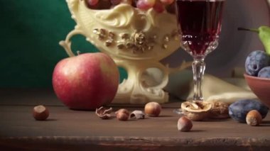 El yapımı kil testisi, vazoda üzümler, erikler, elmalar, fındıklar, armutlar ve bir bardak şarapla hayat.