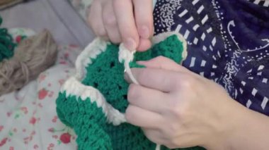 Beyaz ve yeşil yün iplik ören kadınların ellerini kapat.