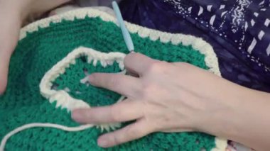 Beyaz ve yeşil yün iplik ören kadınların ellerini kapat.