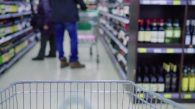 Metal bir yemek arabası süpermarkette duruyor, rafların arasında.