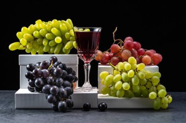 Koyu arkaplanda bir bardak şarapla yeşil ve kırmızı üzümler..