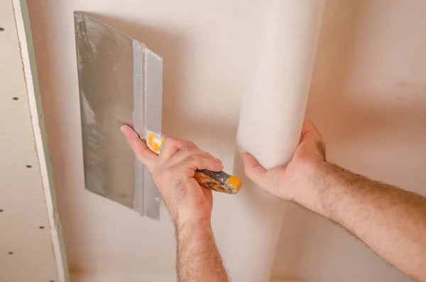 The Builder puts plaster on the wall.Hand holding a spatula with construction mix and smoothes out bumps.Repair the wall.Plaster the wall with a putty knife.