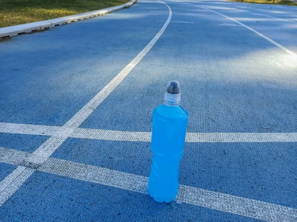 Bebida energética isotónica. Botella con líquido transparente blu, bebida deportiva en un campo de deportes. Inicio para correr . — Foto de Stock