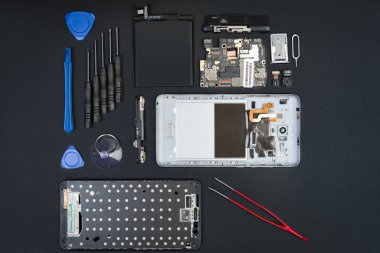 Demonte smartphone ile kaldırılan perde ve özel amaçlı araçlar üstünde siyah okul sırası. Flatlay stil ayrıntılarda cep telefonu.