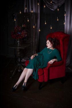 Genç güzel kızıl saçlı beyaz bir kadınla yeşil elbiseli kırmızı kanepede poz profesyonel makyaj