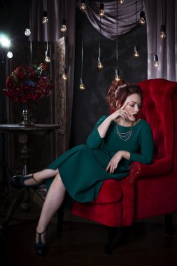 Genç güzel kızıl saçlı beyaz bir kadınla yeşil elbiseli kırmızı kanepede poz profesyonel makyaj