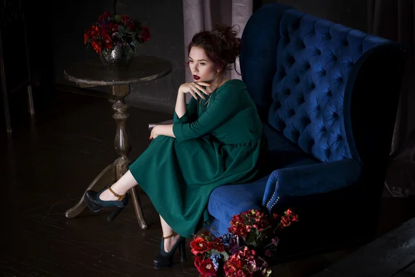Mladá krásná rusovlasá Kavkazský žena s profesionální make-up v zelených šatech pózuje na modré pohovce — Stock fotografie