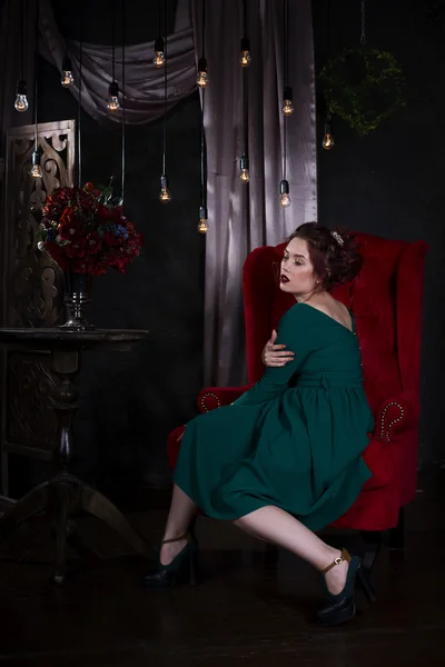 Młoda piękna Rudowłosa kaukaski kobieta z profesjonalny makijaż w zielonej sukni, pozowanie na czerwonej kanapie — Zdjęcie stockowe