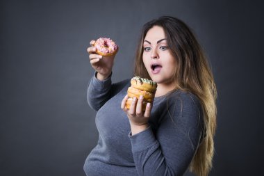 Beautiful young caucasian plus size model posing with donuts on a gray studio background clipart