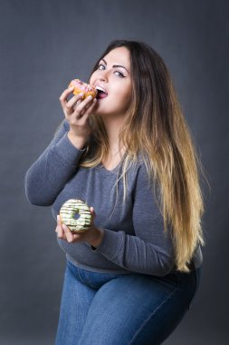 Happy beautiful young caucasian plus size model posing with donuts on a gray studio background clipart