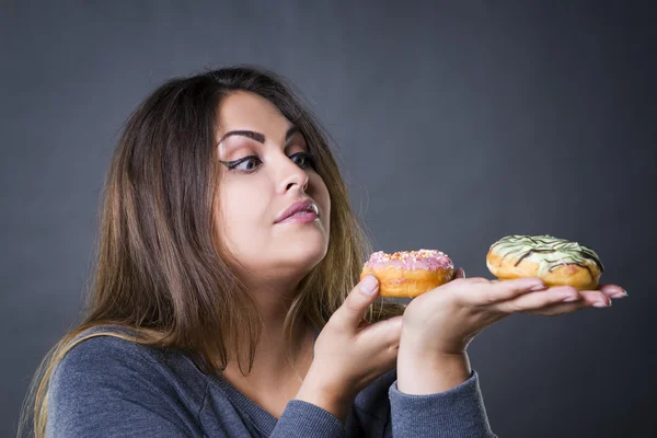 Schönes junges kaukasisches Plus-Size-Model posiert mit Donuts auf grauem Studiohintergrund — Stockfoto