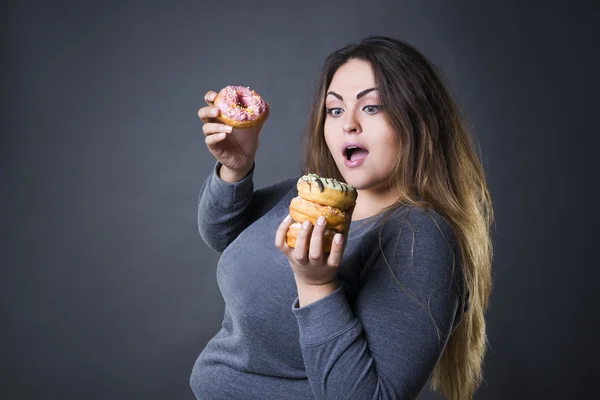 Schönes junges kaukasisches Plus-Size-Model posiert mit Donuts auf grauem Studiohintergrund — Stockfoto
