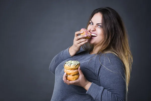 Glücklich schöne junge kaukasische Plus-Size-Model posiert mit Donuts auf einem grauen Studiohintergrund — Stockfoto