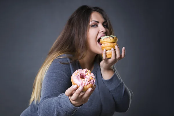 Glücklich schöne junge kaukasische Plus-Size-Model posiert mit Donuts auf einem grauen Studiohintergrund — Stockfoto