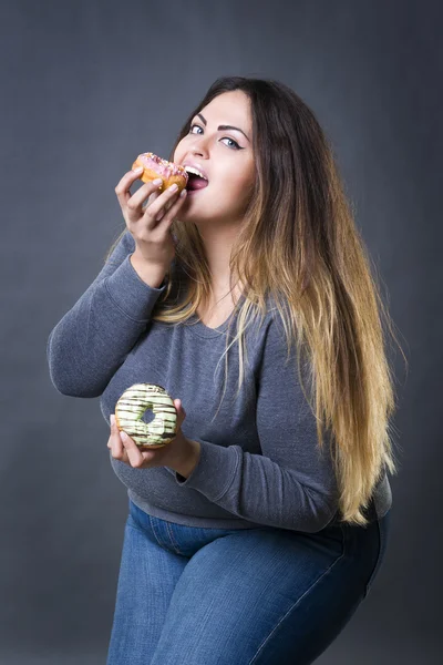 Feliz hermosa joven caucásico más modelo de tamaño posando con rosquillas en un fondo de estudio gris — Foto de Stock