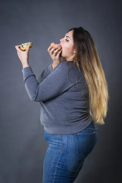 Hermosa joven caucásico más modelo de tamaño posando con rosquillas en un fondo de estudio gris — Foto de Stock