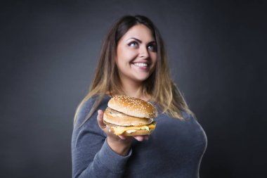 Mutlu güzel genç artı boyutu model xxl kadın hamburger yeme hamburger bir gri studio arka planda ile poz