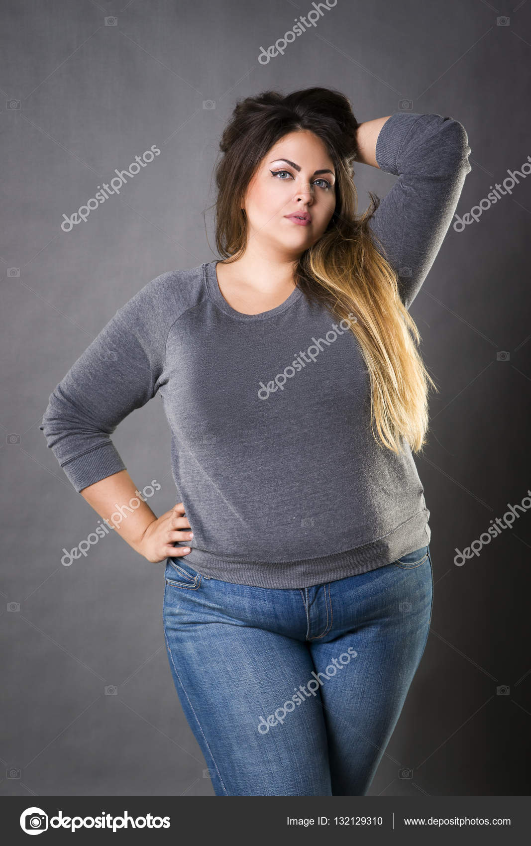 Young beautiful plus size model in blue jeans, xxl woman on gray