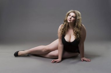 Young beautiful blonde plus size model with big natural breasts in underwear, xxl woman on gray studio background