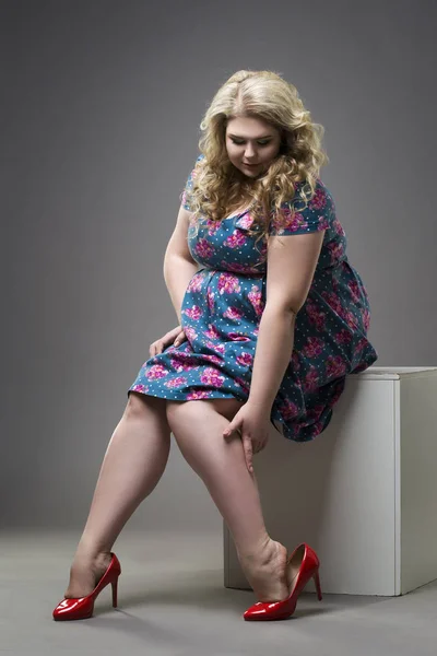 Jonge mooie blonde plus grootte model in rode hoge hakken schoenen, xxl vrouw op grijze achtergrond, benen vermoeidheid — Stockfoto