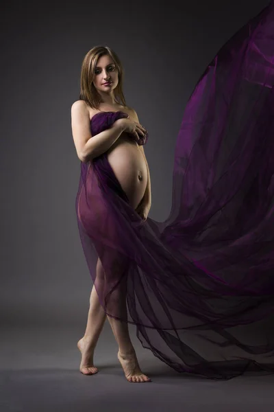 Hermosa mujer embarazada desnuda con seda púrpura sobre fondo gris, concepto de embarazo desnudo — Foto de Stock