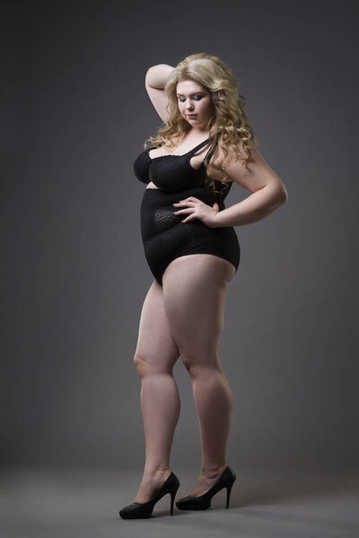Young beautiful blonde plus size model in shapewear, xxl woman in slimming underwear on gray studio background