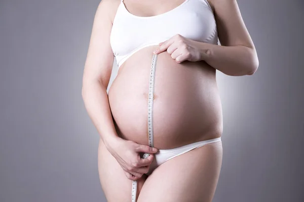 Pregnancy and nutrition - pregnant woman with measuring tape on gray background