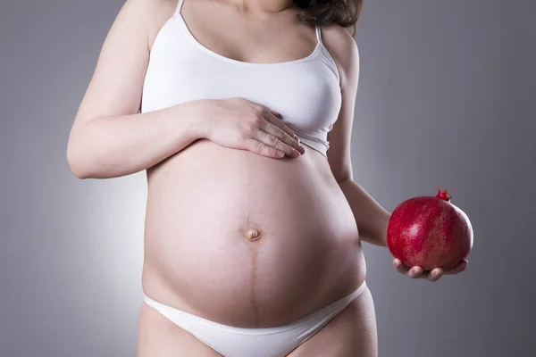 Pregnancy and nutrition - pregnant woman with pomegranate in hand on gray background, vegetarian diet — Stock Photo, Image