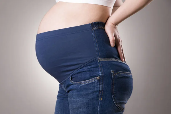 Gravid kvinna i blå jeans för gravida på grå bakgrund — Stockfoto