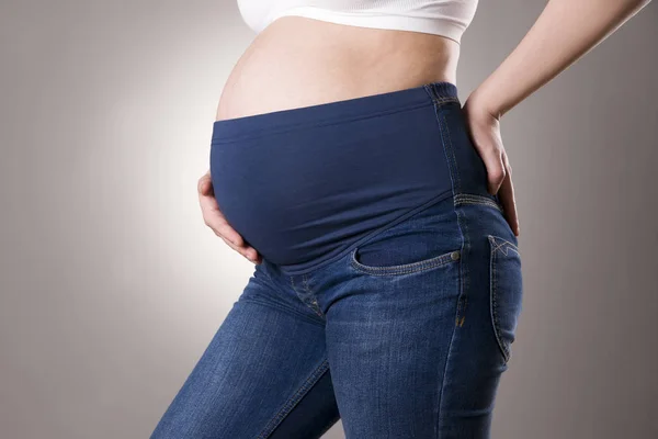 Mulher grávida em jeans azul para mulheres grávidas em fundo cinza — Fotografia de Stock