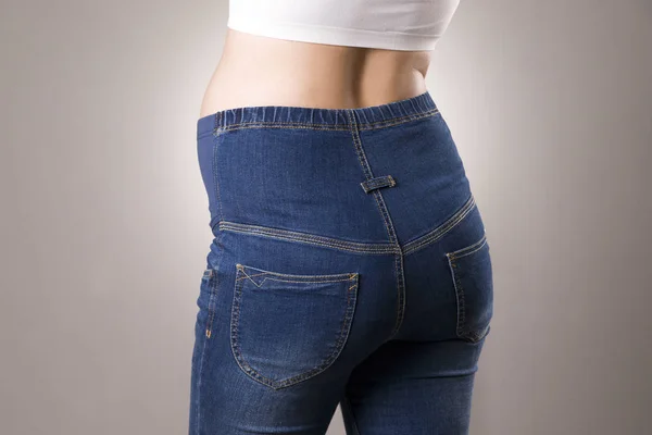 Mujer embarazada en jeans azules para mujeres embarazadas sobre fondo gris —  Fotos de Stock