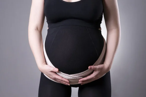 Zwangere vrouw in zwarte panty's met orthopedische ondersteuning gordel, zwangerschap pleister — Stockfoto